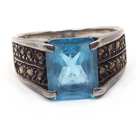Front view of the retro vintage sterling silver marcasite ring with blue rhinestone. The silver is slightly darkened from age. The top of the ring has a large princess cut square blue rhinestone. There are two rows of small round marcasite stones set on each side. All stones are prong set.