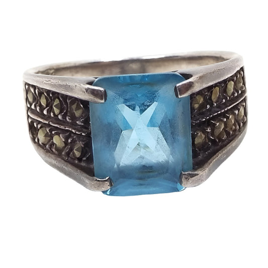 Front view of the retro vintage sterling silver marcasite ring with blue rhinestone. The silver is slightly darkened from age. The top of the ring has a large princess cut square blue rhinestone. There are two rows of small round marcasite stones set on each side. All stones are prong set.