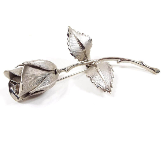 Front view of the retro vintage Giovanni rose brooch. It is silver tone in color and is shaped like a single rose with two leaves. The design is textured on the leaves and petals and has a 3D shape.