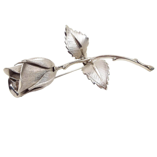 Front view of the retro vintage Giovanni rose brooch. It is silver tone in color and is shaped like a single rose with two leaves. The design is textured on the leaves and petals and has a 3D shape.