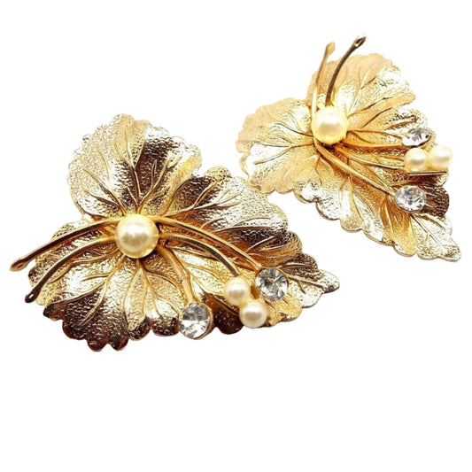 Front view of the Mid Century vintage leaf clip on earrings. They are gold tone in color and are textured. There are three faux pearls in off white color and two clear rhinestones on each leaf.