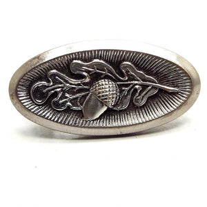 Front view of the Mid Century vintage small tie clip. The metal is antiqued silver tone in color. There is a textured line design in the middle of the oval shape and a raised leaf and acorn in the middle. There is some wear to the silver tone plating on the edge when viewed closely.