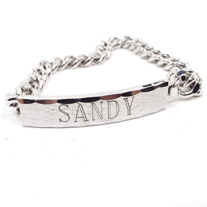 Front view of the retro vintage Speidel ID bracelet. It is silver tone in color. The front curved bar has a brushed matte front with the name Sandy engraved on it. The top and bottom edge are faceted.