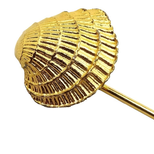 Enlarged view of the top of the retro vintage seashell stick pin. The metal is gold tone in color. The shall is a curved flatter style with lines and ripples. 