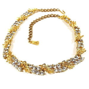 Front view of the Mid Century vintage BSK rhinestone link necklace. The metal is gold tone in color. Each link has a leaf like design and a cluster of six round clear rhinestones. There is a hook clasp at the end. The end chain is darker gold color than the rest of the necklace.