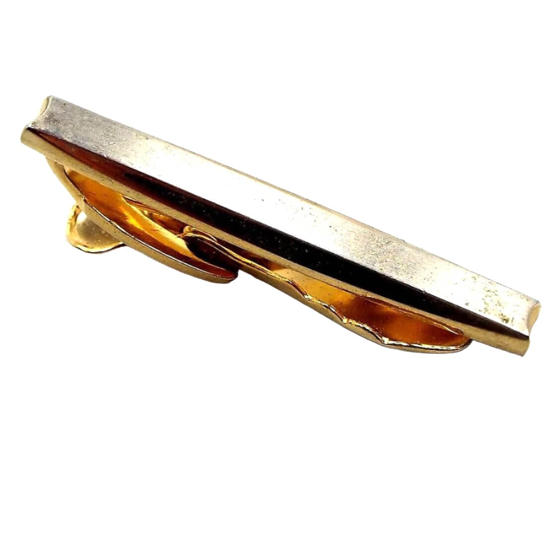 Angled view of the Mid Century vintage Hickok tie clip. It is gold tone in color on the sides and back part of the tie clip. The front is matte silver tone color. Each end has an indented curve. 