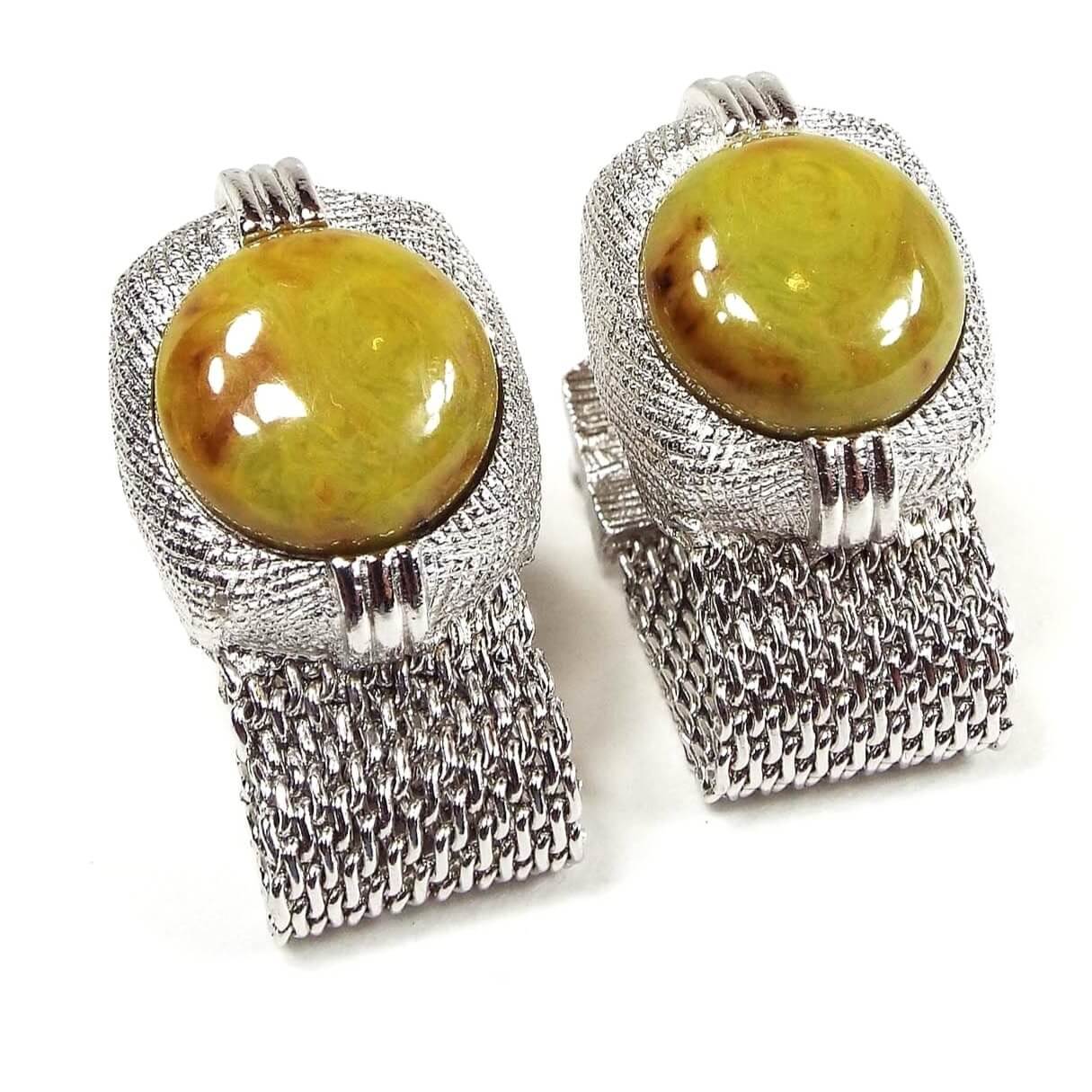 Front view of the Mid Century vintage Swank wrap around cufflinks. They are silver tone in color with mesh from the bottom that goes around to the back. The top part is textured and has domed oval lucite cabs with marbled shades of yellow, green, and orange. They have a mostly yellow look to them and have an imitation stone like appearance with each one looking different than the other in pattern.
