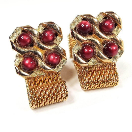 Front view of the Mid Century vintage moonglow lucite wrap around cufflinks. The metal is gold tone in color. There is a four leaf clover style shape at the top with each one having a domed round red moonglow lucite cab in the middle. The lucite has shades of dark red to pink. The mesh chain at the bottom goes around to the back of the cufflinks.