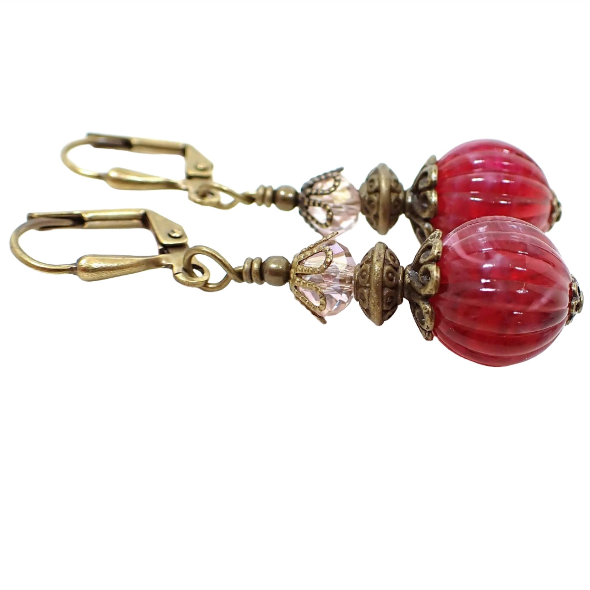 Side view of the handmade raspberry lucite drop earrings. The metal is antiqued brass in color. There is a very light pink faceted glass crystal bead at the top. The bottom lucite beads are round and corrugated with marbled swirls of pink and purple.