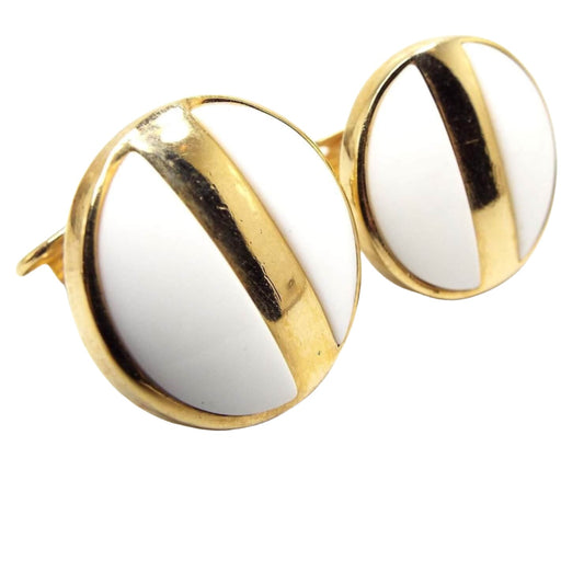 Front view of the retro vintage  Avon earrings. The metal is gold tone in color. They are round with white plastic inserts and a gold tone metal stripe across the middle.