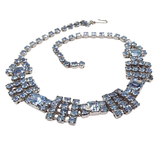 Front view of the Mid Century vintage rhinestone choker necklace. The metal is silver tone in color. The rhinestones are all prong cup chain prong set and are light blue in color. The bottom design has a cluster of rhinestones in a square shape with a cluster in a rectangle shape in between. There is a hook clasp at the end. 