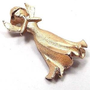 Front view of the 1980's retro vintage Christian Angel brooch pin. The metal is matte gold tone in color. It is an angel with flared bottom dress, small wings, and hands together in prayer. The face is styled to have little detail except a light indent for eyes and mouth. The edges are cut faceted.