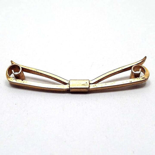 Top view of the 1930's Art Deco vintage collar clip. It is brass metal that is a darker gold tone in color. The front has a bar with curled ends that spiral inward. The back has an angled bar that has slight curves at the ends. Both bars are held together with a rectangular middle area. There are some tiny dark spots on the metal from age.