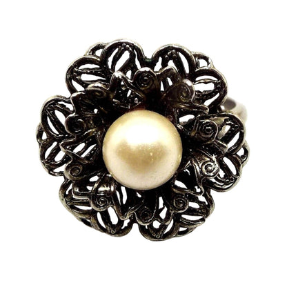 Picture of the top of the adjustable ring. Top has a filigree floral design with two layers of petals. In the middle is a large imitation pearl in an off white color.
