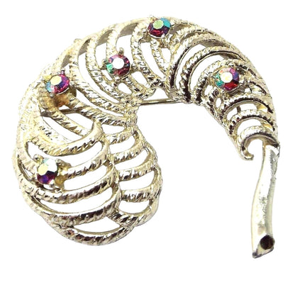 Brooch is gold in color. It has a stem on the right and a curved feather like design on the left. The feather design has cut out filigree areas and 5 randomly placed rhinestones that are AB red in color. The aurora borealis red is a reddish pink in color with flashes of other colors as you move around.