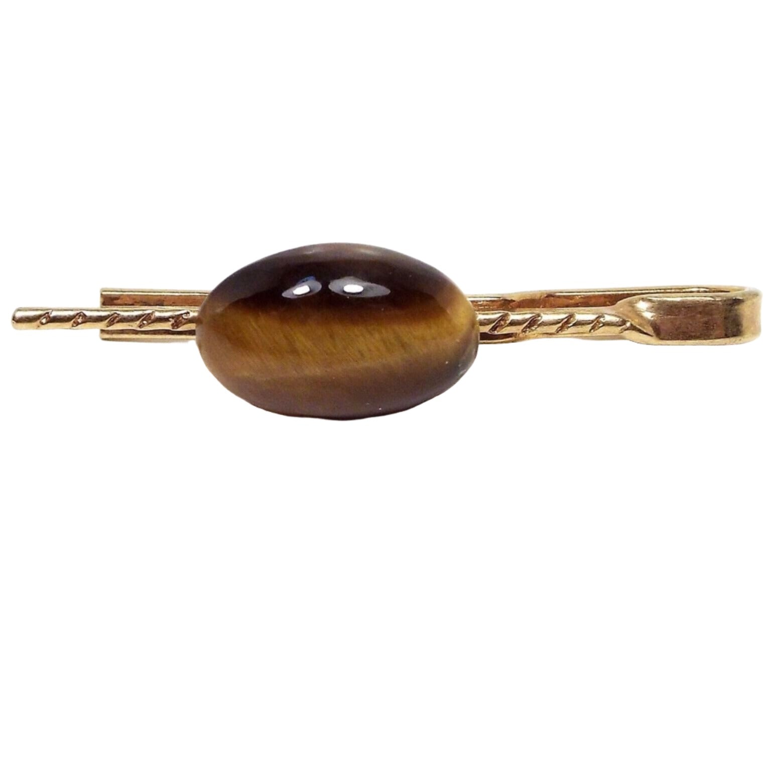 Front view of the retro vintage slide on gemstone tie bar. The metal is gold tone in color. The front has a thin metal bar with a diagonal line etched design on it. The bar flattens at the end and curves around the back of the tie bar. There is a domed oval tiger's eye cab attached to the front with striped shades of yellow and brown.