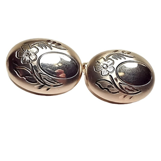Front view of the Mid Century vintage Flex Let Quaility cufflinks. They are puffy oval in shape and are slightly darker gold tone in color. Each cufflinks has and etched oval on the right side of the cufflink. There is a flower design with leaves and stem etched around the edge of the oval on the front. 