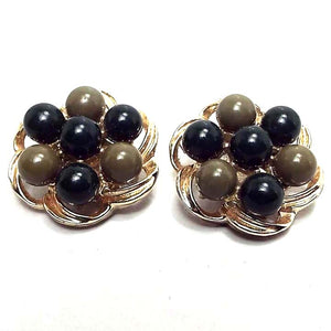 Front view of the Mid Century vintage clip on earrings. The metal is gold tone in color. Each earring has a scalloped open floral like design. There are round beads around the edge alternating between dark green and olive green in color and another dark green bead in the middle. 