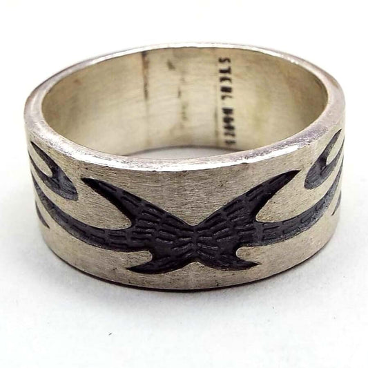 Angled front and side view of the retro vintage sterling silver band ring. The sterling is matte silver in color and the tribal style design is dark gray almost black in color. The design is curvy with spiky ends. Sterling 925 is stamped inside the band. There are some dark areas in side the band from age.