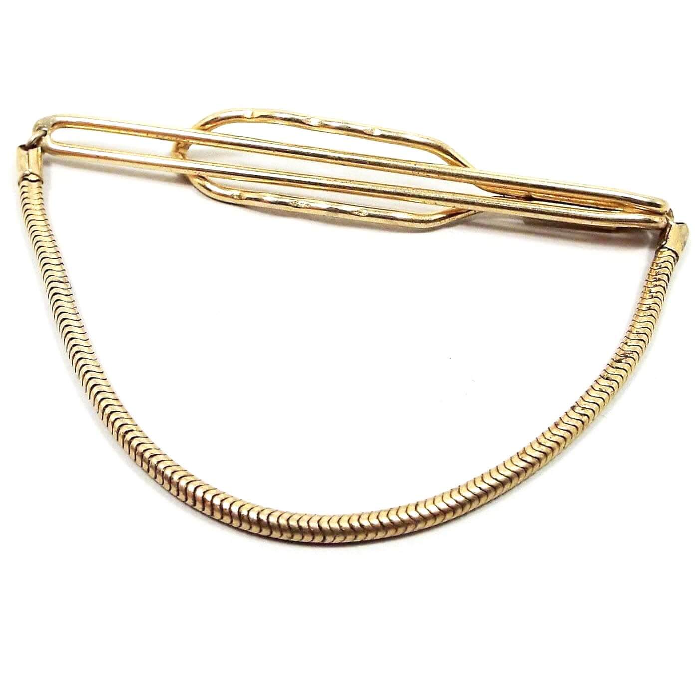 Front view of the Mid Century 1940's vintage Anson tie chain. It is gold tone in color. There is a long open oval bar on the front and a larger but shorter open oval bar on the back to slide the tie in between. There is a round snake link chain at the bottom. 