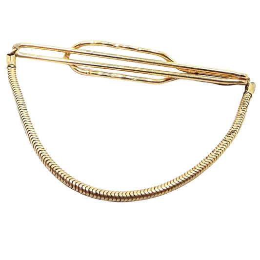 Front view of the Mid Century 1940's vintage Anson tie chain. It is gold tone in color. There is a long open oval bar on the front and a larger but shorter open oval bar on the back to slide the tie in between. There is a round snake link chain at the bottom. 