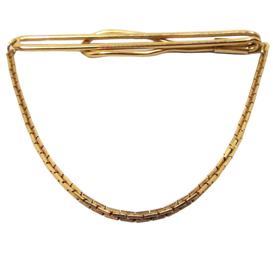 Front view of the 1940's Mid Century vintage Swank tie chain bar. It is gold tone in color. The top has a long open oval wire bar that curves around to the back with a larger open oval area on the end. Square link chain comes down from either side to hang in a curve at the bottom. 