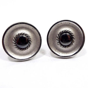 Front view of the Mid Century vintage Anson faux hematite cufflinks. They are round and darkened matte silver in color with smaller round dark metallic gray imitation hematite cabs in the middle. There is a textured round design around the cabs. 