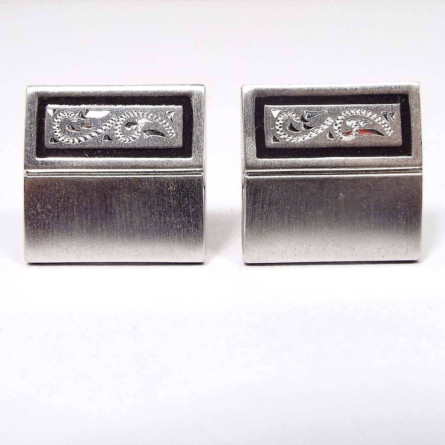 Front view of the Mid Century vintage Speidel cufflinks. They are matte silver tone in color and square shaped. there is a line through the middle of the cufflinks. On the top of the cufflinks is a black painted rectangle with an etched paisley design on the inside.