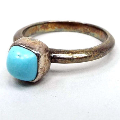 Angled side and front view of the retro vintage sterling silver imitation turquoise ring. The silver is darkened from age to a gray color. The top has a rounded square glass cab that is domed at the top. 