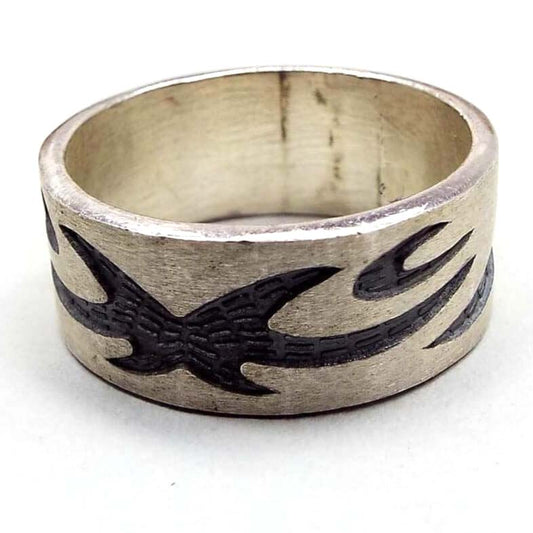 Angled front and side view of the retro vintage sterling silver band ring. The sterling is matte silver in color and the tribal style design is dark gray almost black in color. The design is curvy with spiky ends. There are some dark areas in side the band from age.