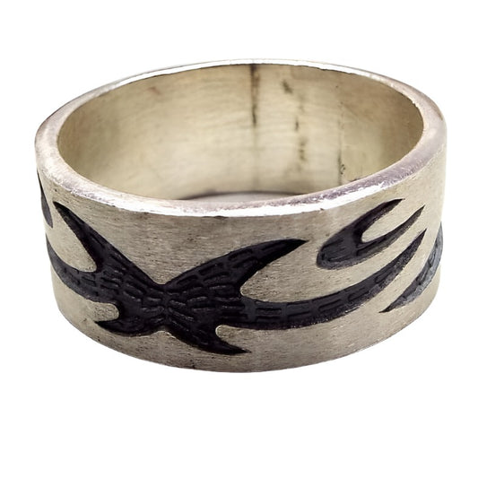 Angled front and side view of the retro vintage sterling silver band ring. The sterling is matte silver in color and the tribal style design is dark gray almost black in color. The design is curvy with spiky ends. There are some dark areas in side the band from age.