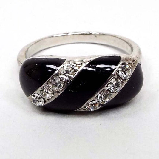 Top view of the retro vintage rhinestone ring. The metal band and setting is silver tone in color. At the top there is a curved oval area with diagonal stripes alternating between shiny black enamel and pavé set rhinestones. The rhinestones are small round shaped and are sparkling clear in color. 