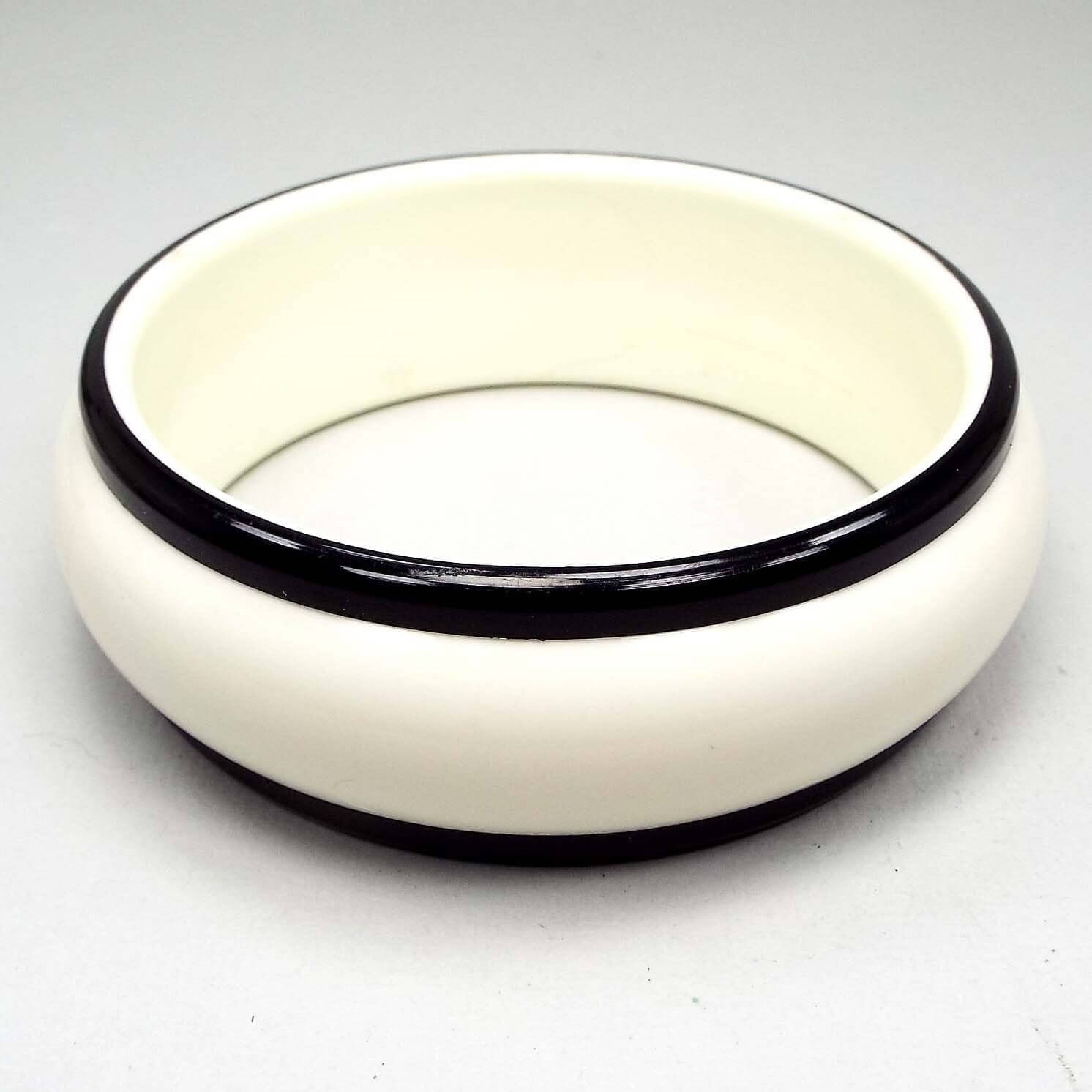 Side view of the Mid Century vintage bangle bracelet. The bangle has a wide design with white plastic and a black plastic trim on each side. It is a round shaped bangle.