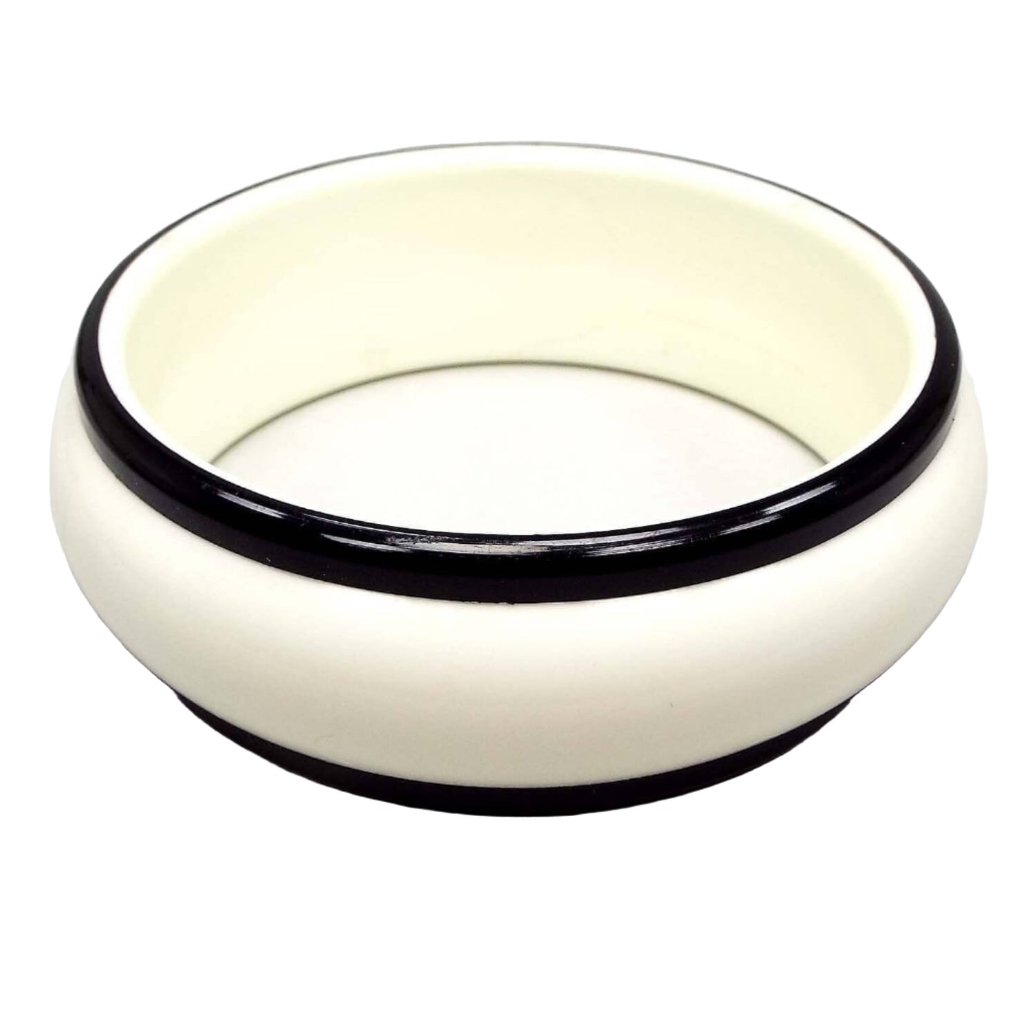 Side view of the Mid Century vintage bangle bracelet. The bangle has a wide design with white plastic and a black plastic trim on each side. It is a round shaped bangle.