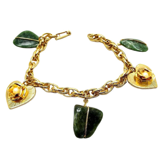 Top view of the retro vintage charm bracelet. The bracelet is gold tone in color and has a textured oval rope chain with a snap lock clasp. The charms alternate between a green flatter style freeform agate gemstone nugget held by a gold tone wire and heart shaped metal charms that have a rose in the middle with plastic faux pearls. 