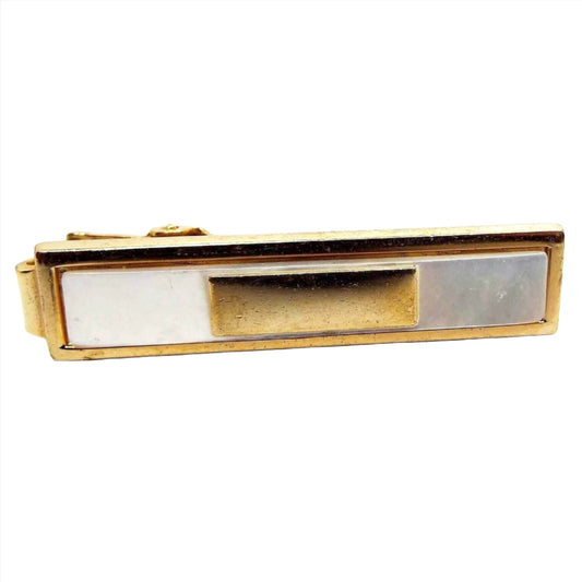 Front view of the Mid Century Anson tie clip. It has a rectangle design. It is gold tone in color with an inlaid rectangle of mother of pearl shell. The shell cab is pearly white in color. Inside the mother of pearl cab is another gold tone color metal rectangle. There is an alligator style clip on the back.