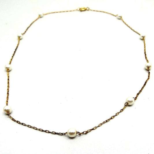 Front view of the retro vintage faux pearl beaded chain necklace. The chain is thin oval cable link and gold tone in color. There is a spring ring clasp at the end. There are nine small round off white glass imitation pearls spread out along the chain.