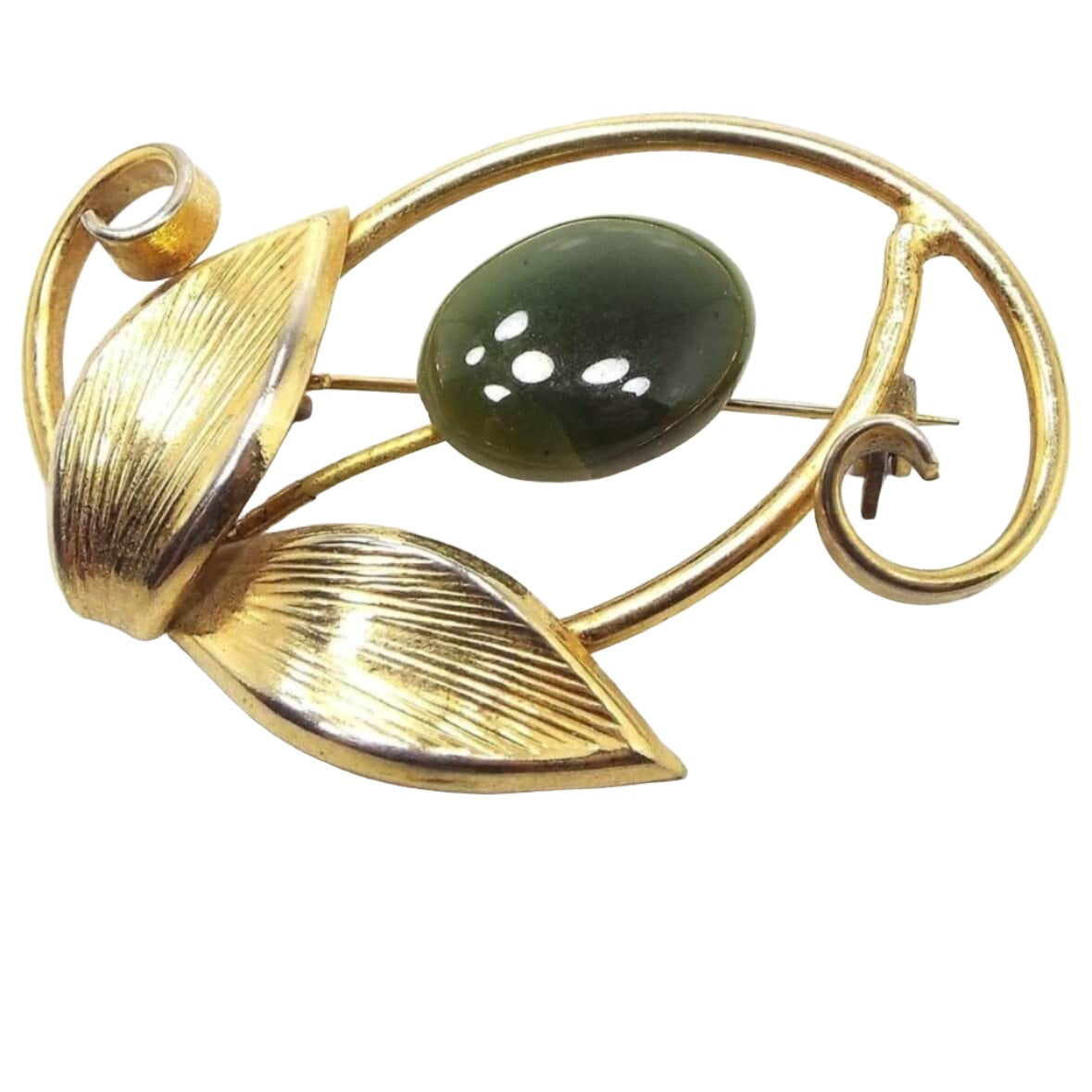 Front view of the retro vintage floral brooch. the metal is gold tone in color. The flower head is a puffy oval green jade gemstone cab. There is a wire stem that goes down to two textured leaves and there are curled areas of metal on each side and around the head of the floor with an open space in between.