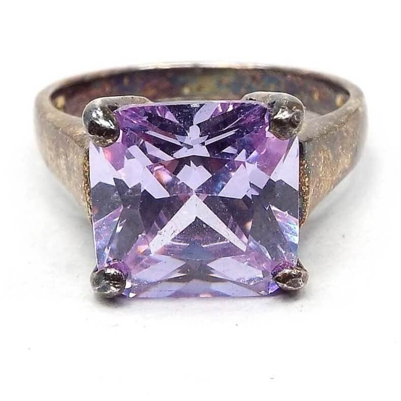 Front view of the top of the retro vintage sterling silver purple cubic zirconia ring. There is a larger sized prong set square cut CZ stone in the middle. It is a light purple in color with hints of lilac and lavender as you move around. The sterling is darkened with age and has some hints of bluing on the inside of the band and the top part by the stone.