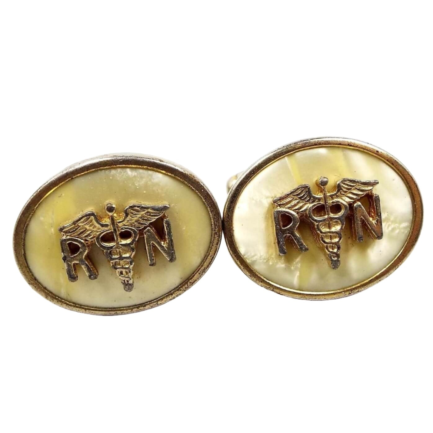 Front view of the Anson Mid Century vintage RN cufflinks. They are oval in shape and the metal is gold tone in color. The inside of the ovals have pearly lucite plastic cabs that are light yellow in color. On top of the lucite cabs is the registered nurse symbol with the letter R and N separated by the Caduceus medical emblem of two snakes entwined around a winged staff. 