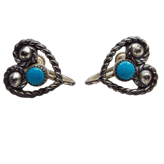 Front view of the retro vintage sterling silver screw back heart earrings. The sterling is darkened from age and is gray in color. There is a twisted wire like design curled at each side on the top to form the open heart shape. There is a small round bezel set cab of stabilized blue turquoise in the middle. 