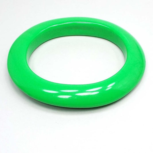 Angled front and side view of the Mid Century vintage lucite bracelet. It's bright green in color and oval shaped. It's fairly wide and thick.