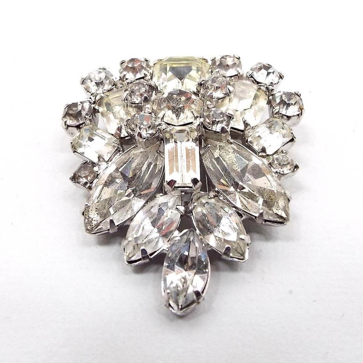 Front view of the 1940's Mid Century vintage rhinestone fur clip. The metal is silver tone in color. It has clusters of prong set clear rhinestones in marquis, round, baguette, and square shapes. The shape of the clip has rounded top sides and comes down to a point at the bottom.