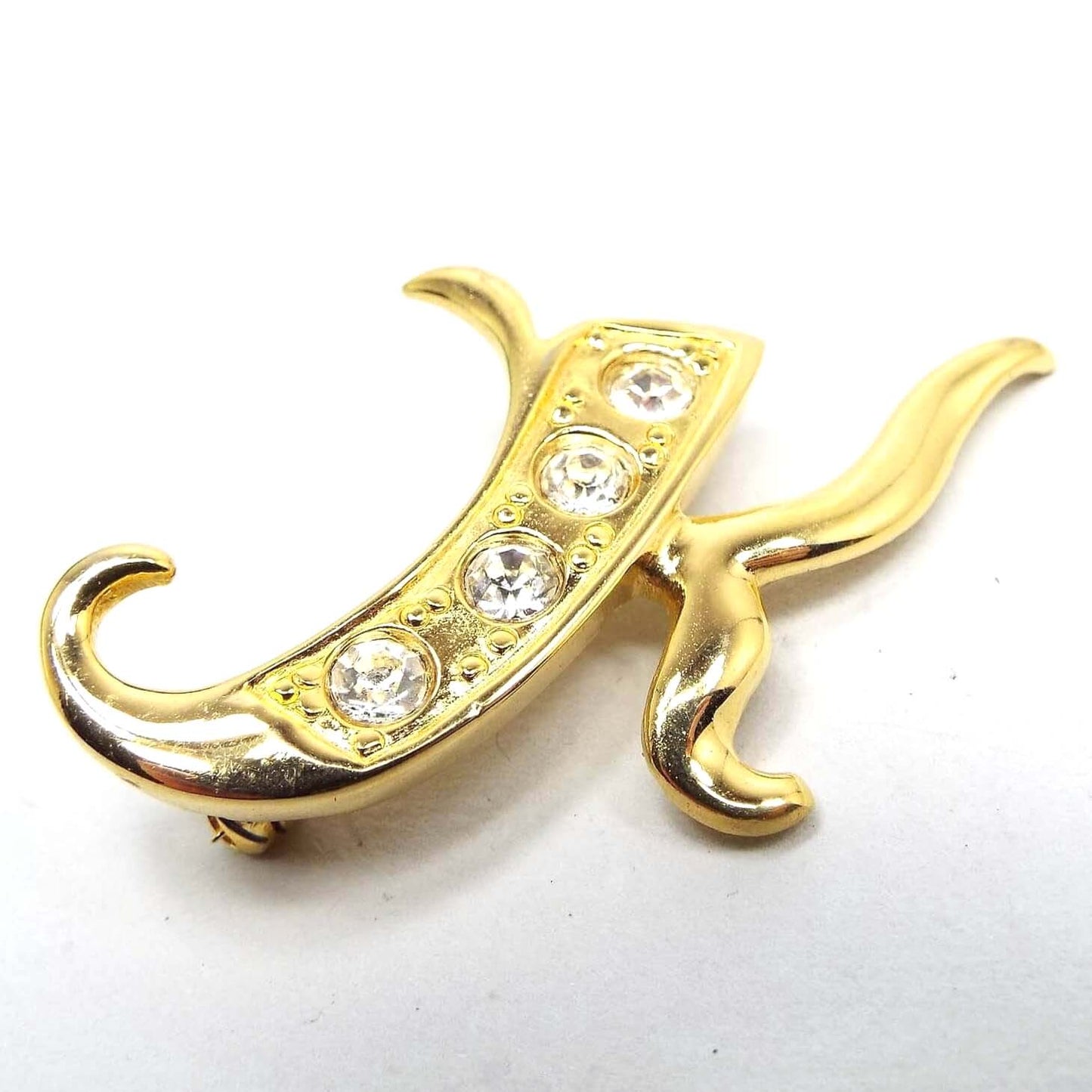Front view of the retro vintage rhinestone initial brooch pin. The brooch is shaped like a curvy initial letter K and has four clear round rhinestones on the left part of the brooch.