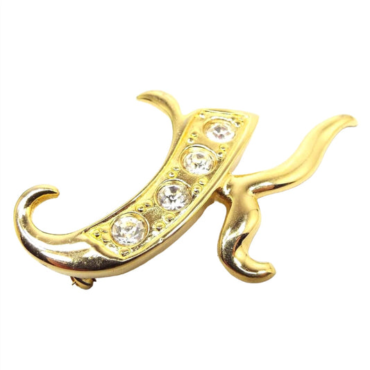 Front view of the retro vintage rhinestone initial brooch pin. The brooch is shaped like a curvy initial letter K and has four clear round rhinestones on the left part of the brooch.