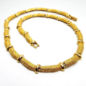 Top view of the retro vintage Avon link necklace from the 1980's. It has dot textured slightly curved links with metal disc beads in between. There is a snap lock clasp on the end. The metal is gold tone in color. 