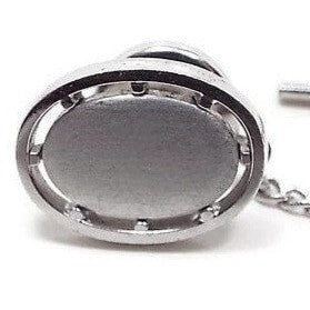 Front view of the Mid Century vintage tie tack. It is oval in shape with a matte silver tone color front. There is a cut out area around it that has small dots spaced out around the middle edge.