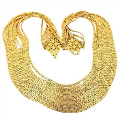 Front view of the Mid Century vintage D'Orlan multi strand chain necklace. There are 11 strands of C link chain in graduating lengths. The chain is flat and has 2 rows of interlocking curve links on each side of the chain. The ends of the necklace attach with small jump rings to an area that has a large diamond pattern. The diamond pattern has 8 smaller diamond shapes inside it that is textured with lines. At the end of each diamond pattern is part of the snap lock clasp. 