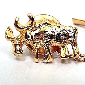 Front view of the Mid Century vintage moose tie tack. The metal is gold tone in color. The front has a textured semi 3D side view of two moose standing side by side. the one in the back has his head down some. Both have antlers. The rounded clutch on the back has a curb chain going to a small bar at the end.