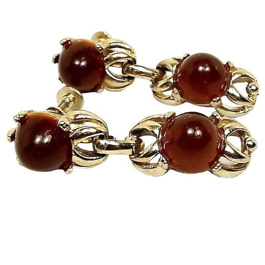 Front view of the retro vintage screw back earrings. Settings are gold tone in color. Top part of the earrings have prong set domed round burnt orange lucite plastic cabs. Underneath are two U shaped metal areas, one inside the other, with a link attached to the bottom for the drop to dangle from. The drops have the open metal areas on the top and bottom and have another domed round burnt orange lucite cab in the middle of them.